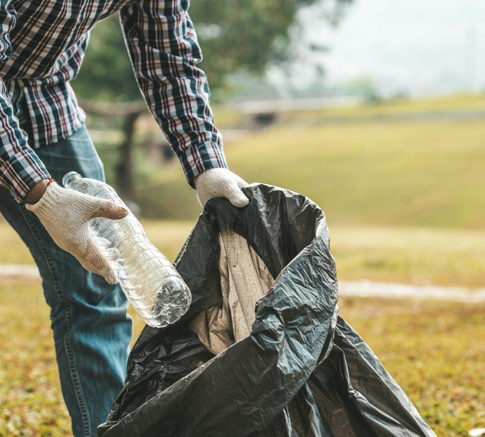 A man is picking up trash in a park, not throwing trash in the trash can ruin the beauty.